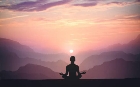 Man practices yoga and meditates on the mountain and sunset